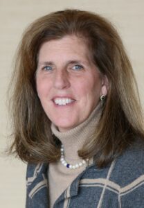 woman with light brown hair wearing a beige turtleneck and plaid jacket smiling for camera