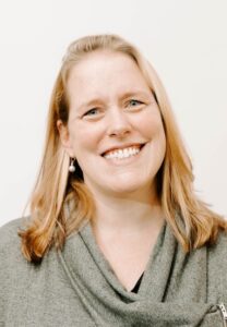 woman with strawberry blonde hair wearing gray shirt and smiling 